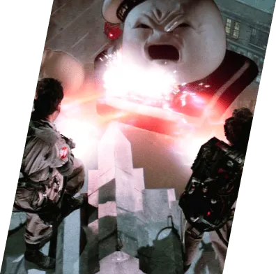 A snippet from the movie Ghostbusters. In the foreground, the Ghostbusters team is trying to defeat the Stay Puft Marshmallow Man as it terrorizes the city. 